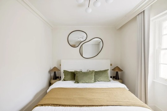 Guest bedroom with sculptural mirrors and green cushions