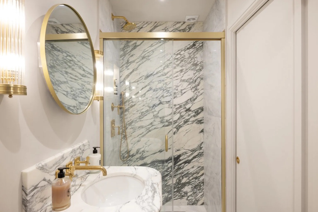Marble shower room with round brass mirror and fluted sconces
