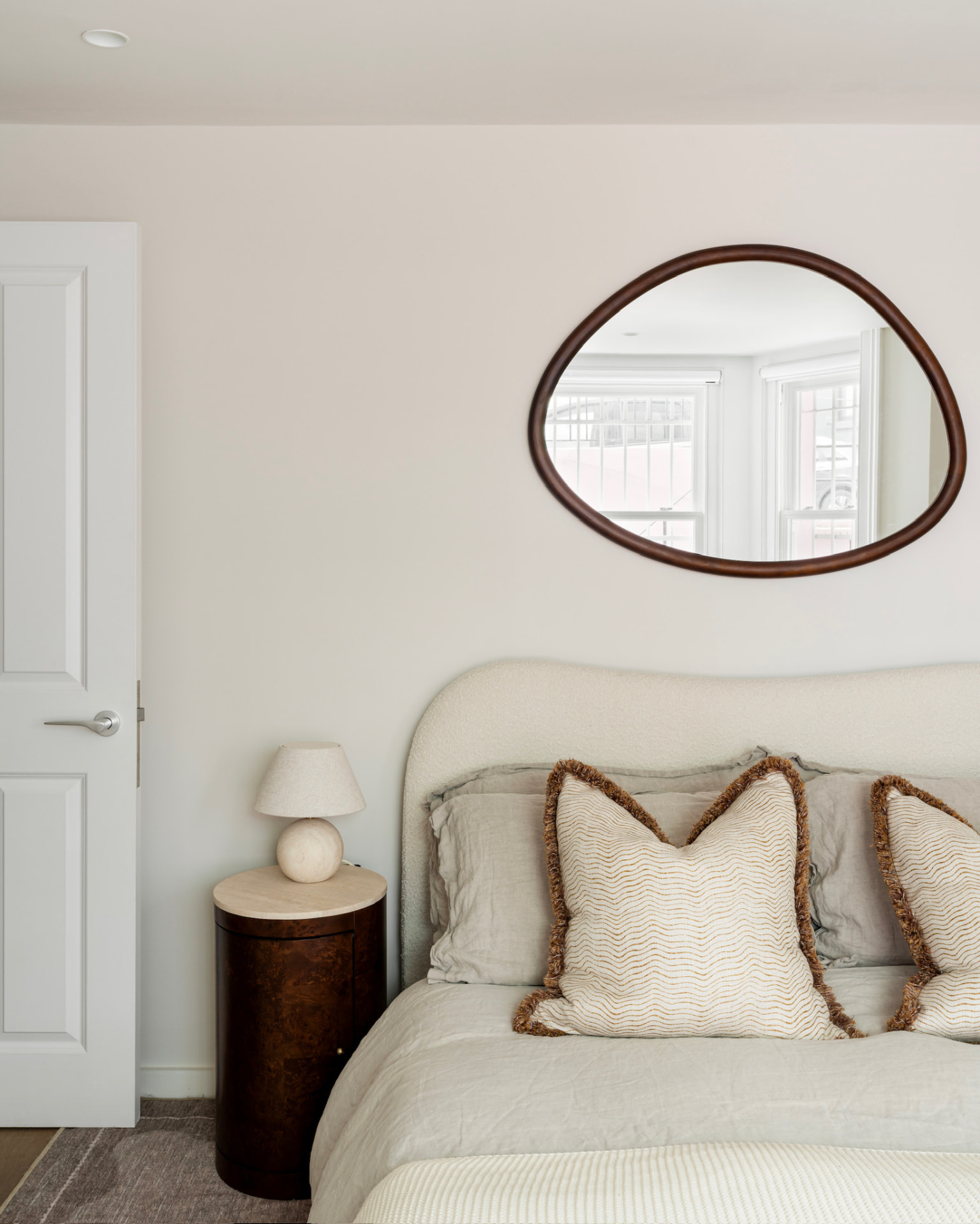 Bedroom with boucle headboard, linen bedding and sculptural mirror