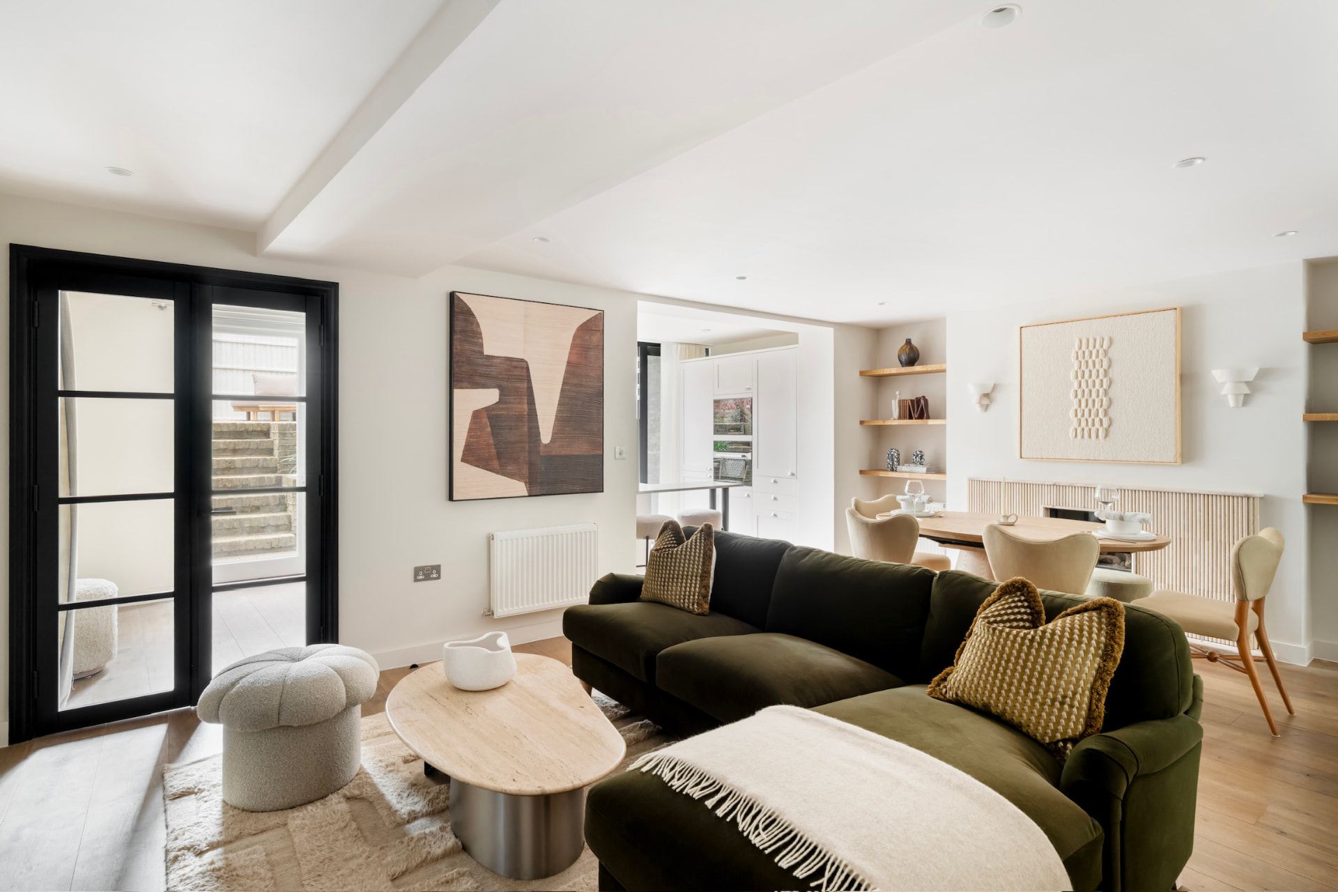 Open-plan living and dining room with deep green sofa and black Crittall garden doors